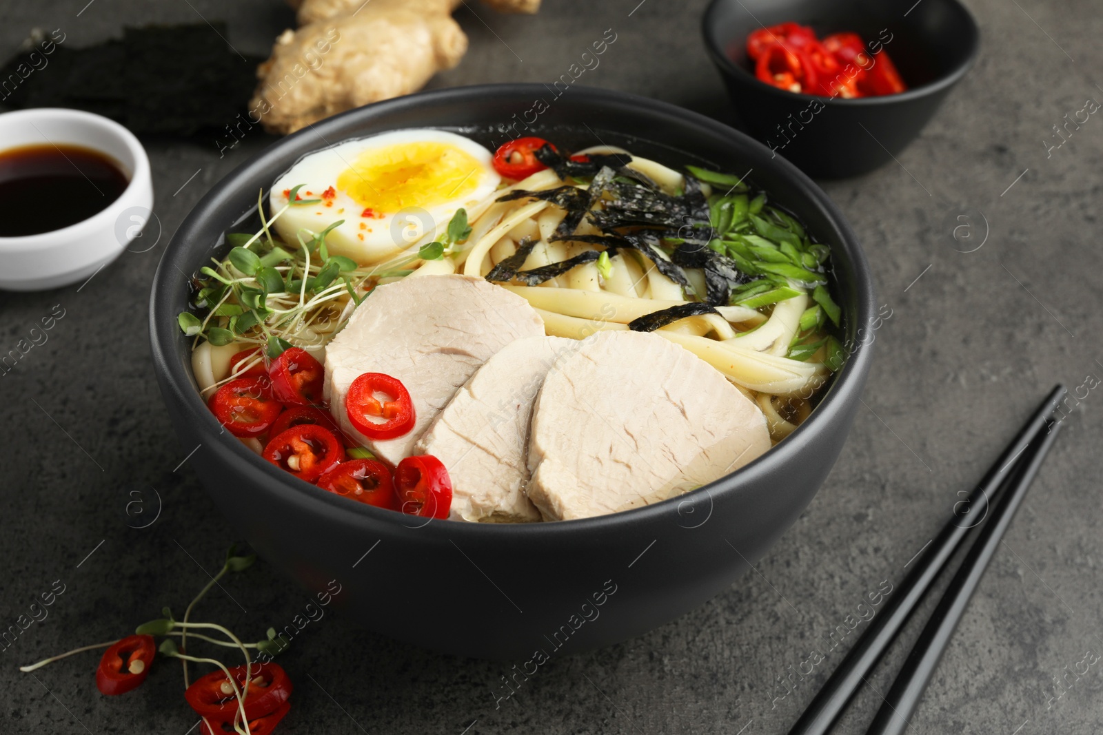 Photo of Delicious ramen with meat in bowl and ingredients on grey textured table, closeup. Noodle soup