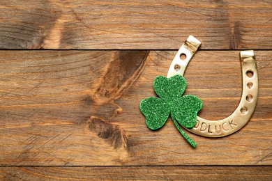 Photo of Golden horseshoe and decorative clover leaf on wooden table, flat lay with space for text. Saint Patrick's Day celebration
