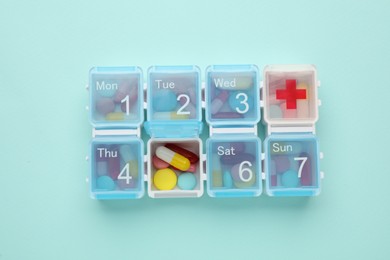 Plastic box with different pills on turquoise background, top view