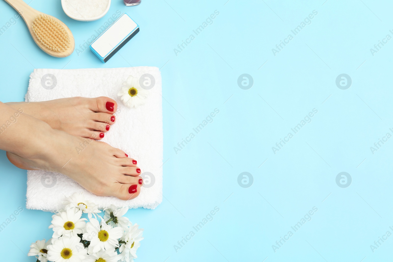 Photo of Woman with stylish red toenails after pedicure procedure and chamomile flowers on light blue background, top view. Space for text