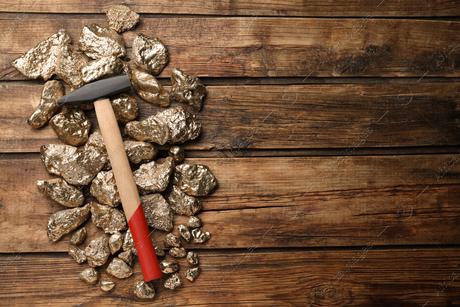 Photo of Pile of gold nuggets and hammer on wooden table, flat lay. Space for text