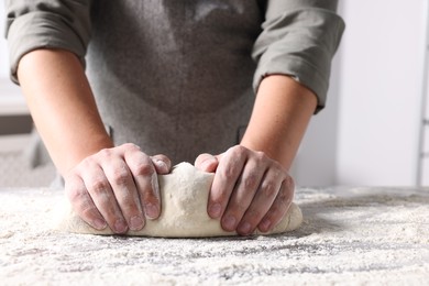 Photo of Man kneading dough at table in kitchen, closeup