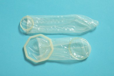 Photo of Unrolled female and male condoms on light blue background, flat lay. Safe sex