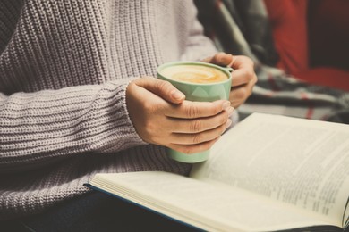 Image of Woman with cup of coffee reading book at home, closeup