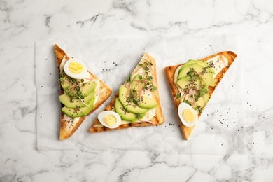 Tasty toasts with avocado, quail eggs and chia seeds on marble background, top view