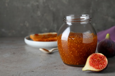 Photo of Delicious fig jam and fresh fruit on grey table. Space for text