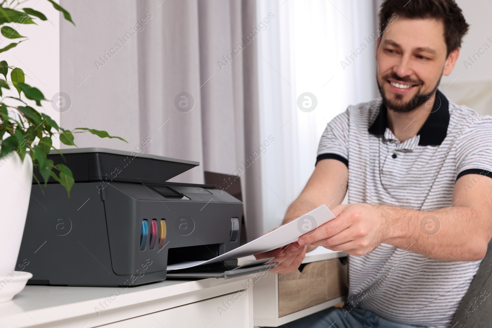 Photo of Man using modern printer at workplace indoors, selective focus