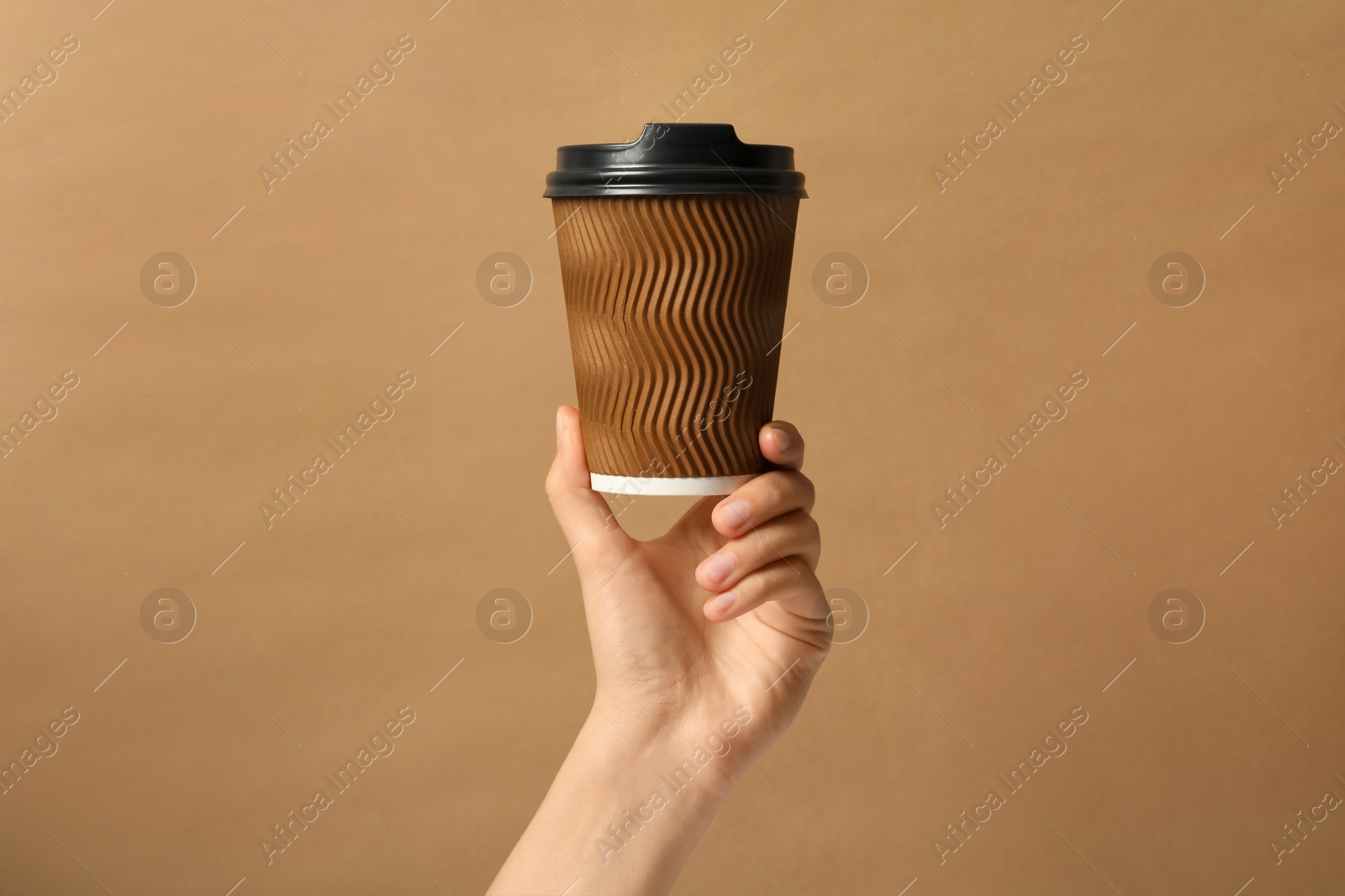 Photo of Woman holding takeaway paper coffee cup on brown background, closeup