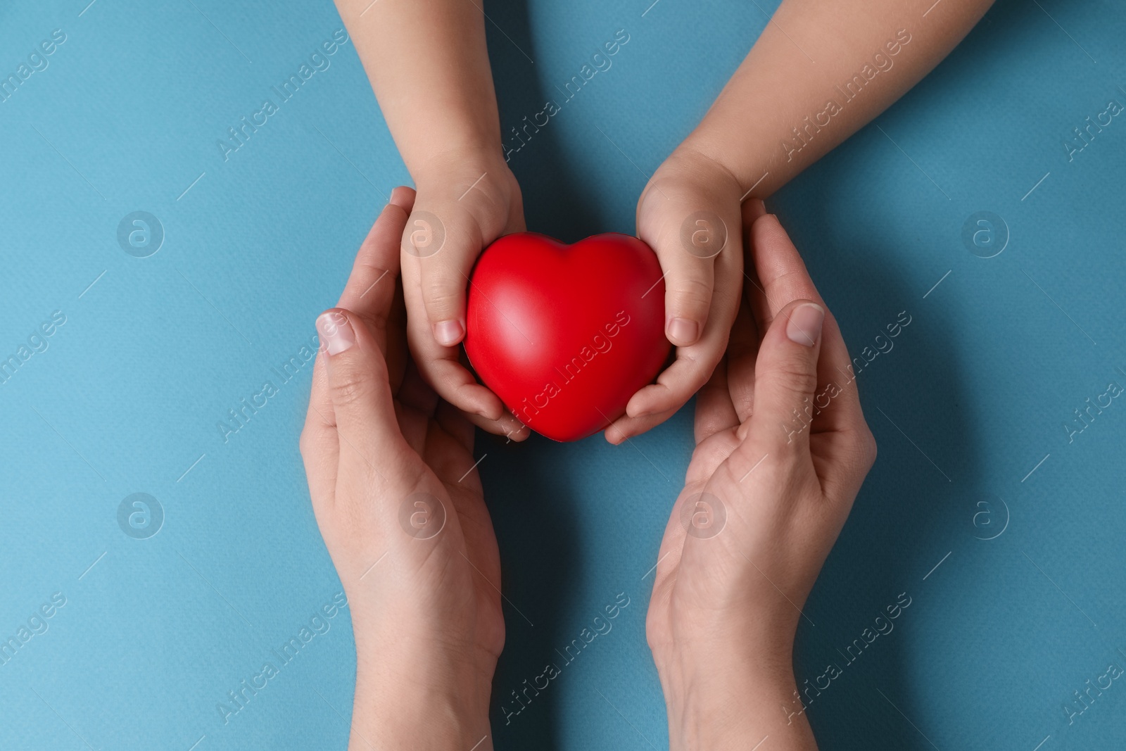 Photo of Mother and her child holding red decorative heart on light blue background, top view