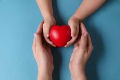 Mother and her child holding red decorative heart on light blue background, top view