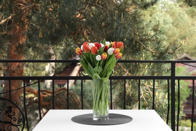 Photo of Beautiful colorful tulips in glass vase on white table at balcony