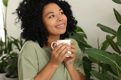 Photo of Relaxing atmosphere. Happy woman with cup of hot drink near beautiful houseplants