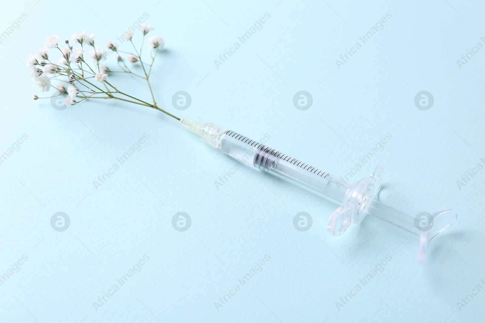 Photo of Cosmetology. Medical syringe and gypsophila on light blue background