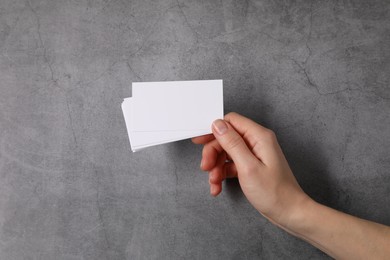 Photo of Woman holding blank cards at grey table, top view. Mockup for design