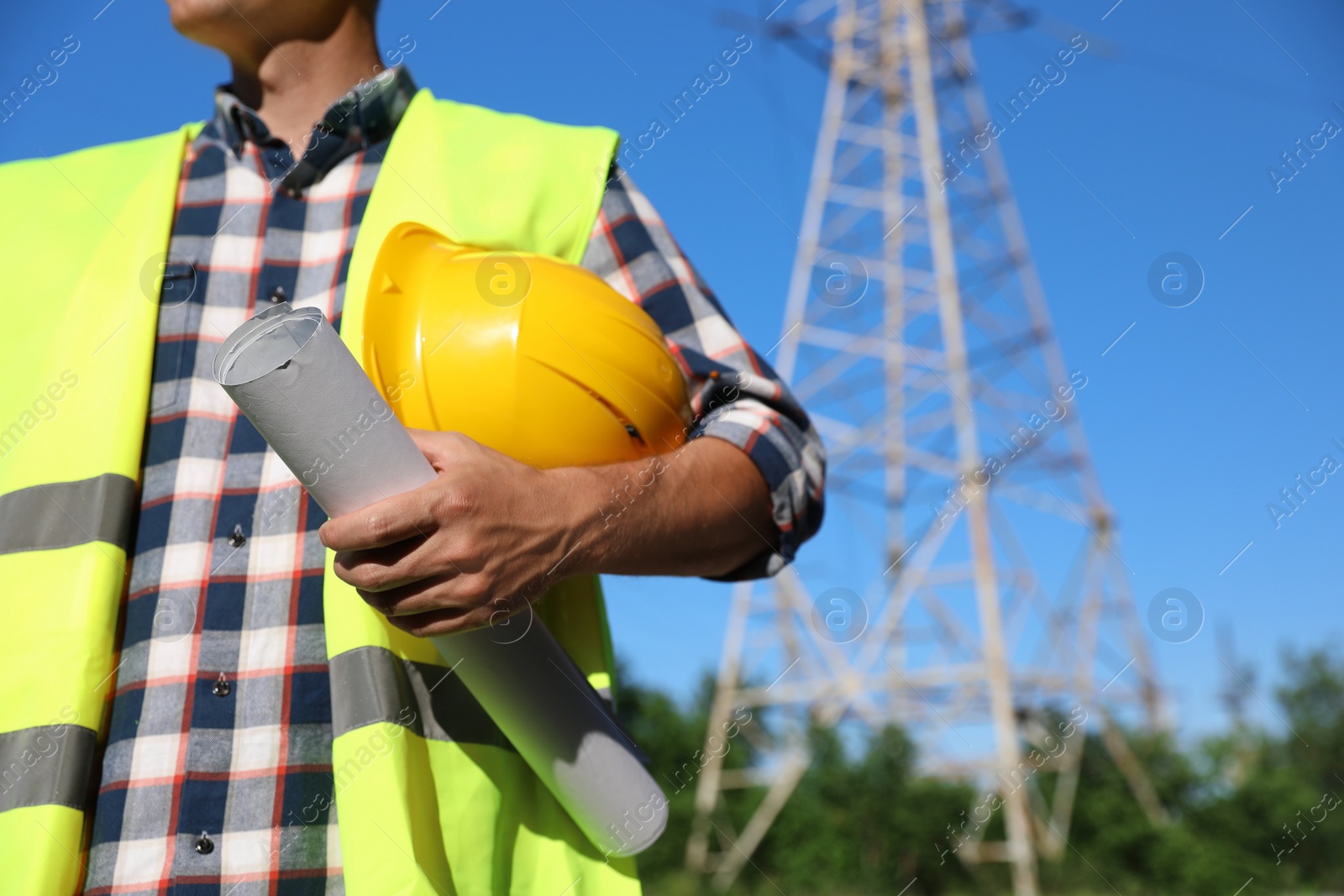 Photo of Professional electrician with drafting and helmet near high voltage tower, closeup