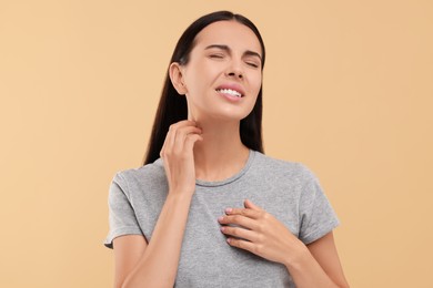 Photo of Suffering from allergy. Young woman scratching her neck on beige background