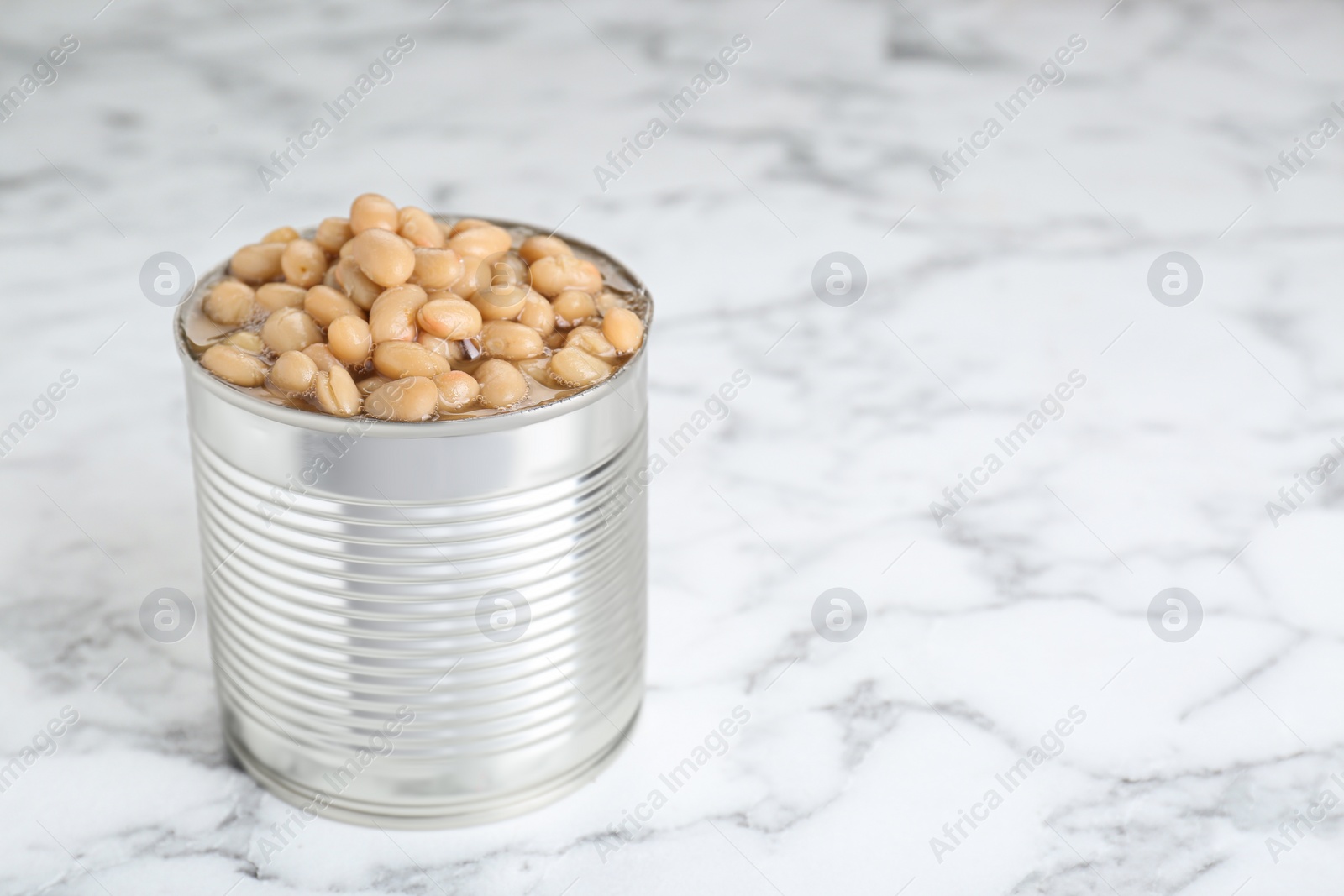 Photo of Tin can with kidney beans on white marble table, space for text