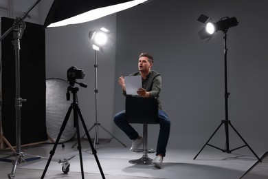 Photo of Casting call. Man with script sitting on chair and performing in front of camera in studio