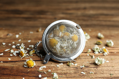 Photo of Dry chamomile flowers in infuser on wooden table, closeup