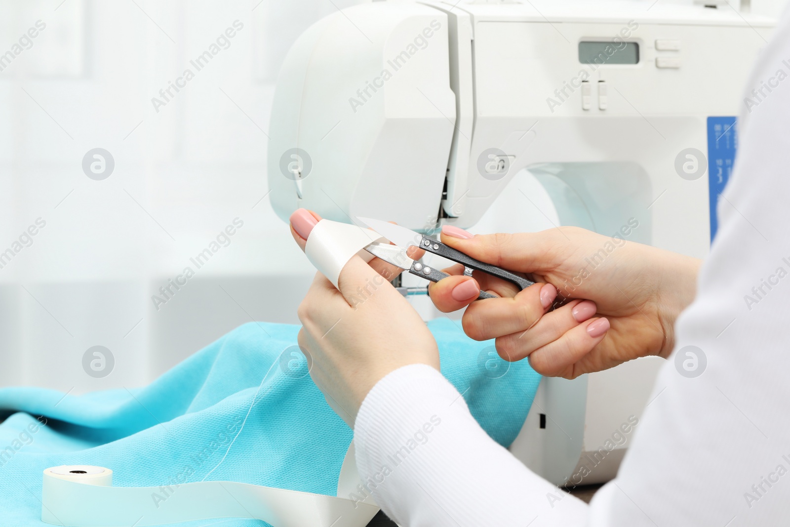 Photo of Seamstress with tailor's scissors working with sewing machine indoors, closeup