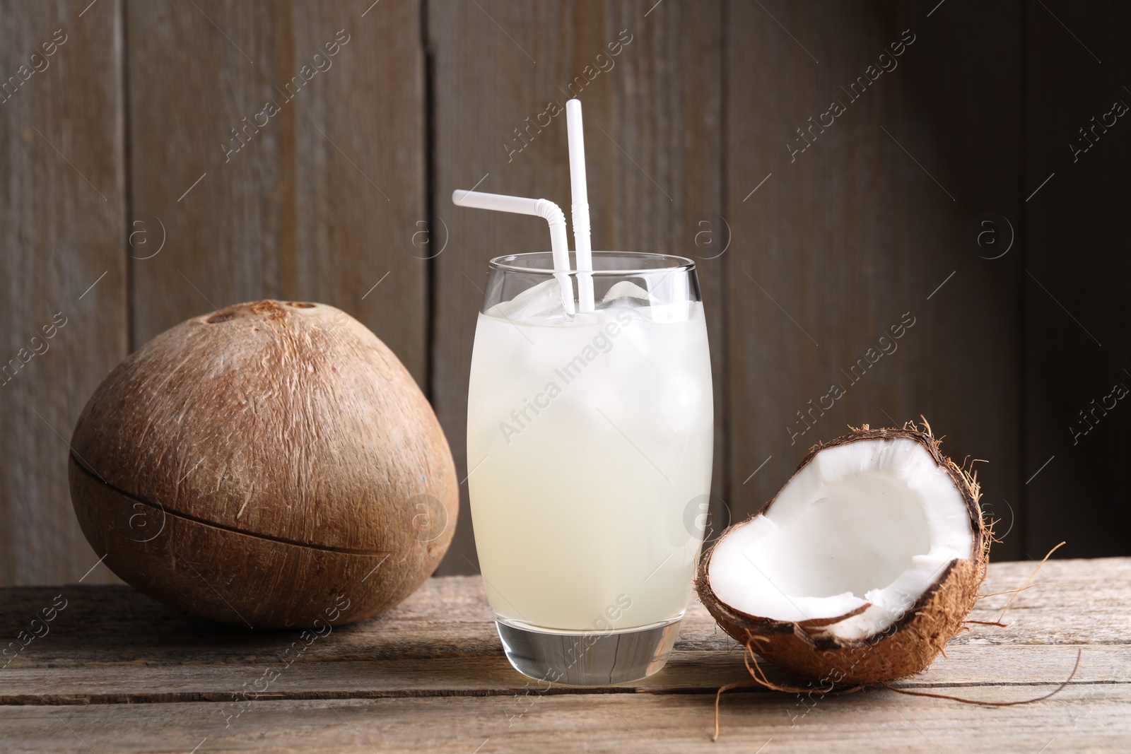 Photo of Glass of coconut water, ice cubes and nuts on wooden table