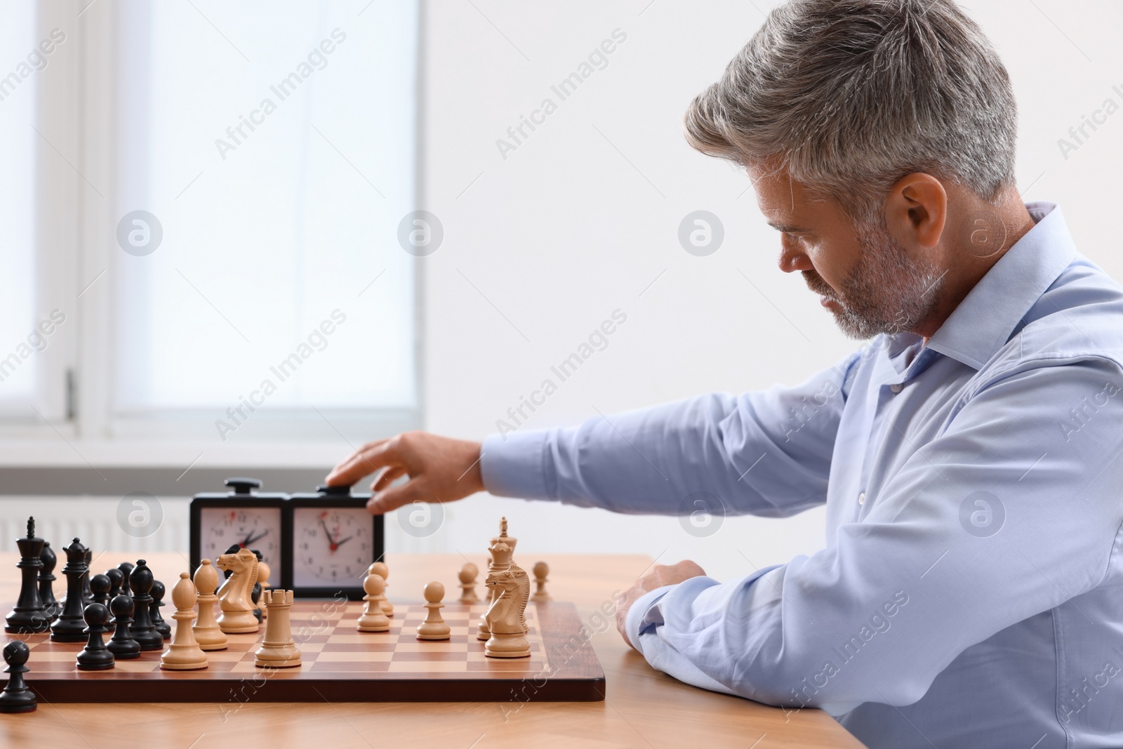 Photo of Man turning on chess clock during tournament at table indoors