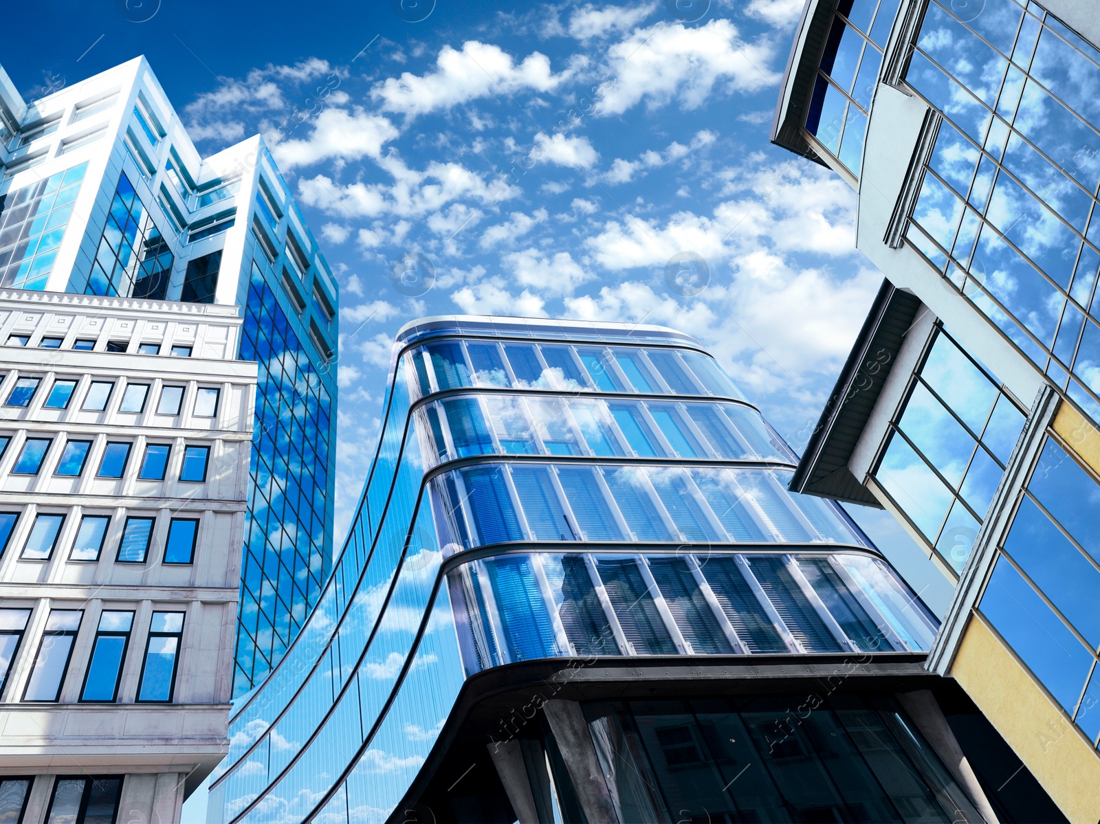 Image of Beautiful blue sky with clouds reflecting in windows of modern buildings. Low angle view