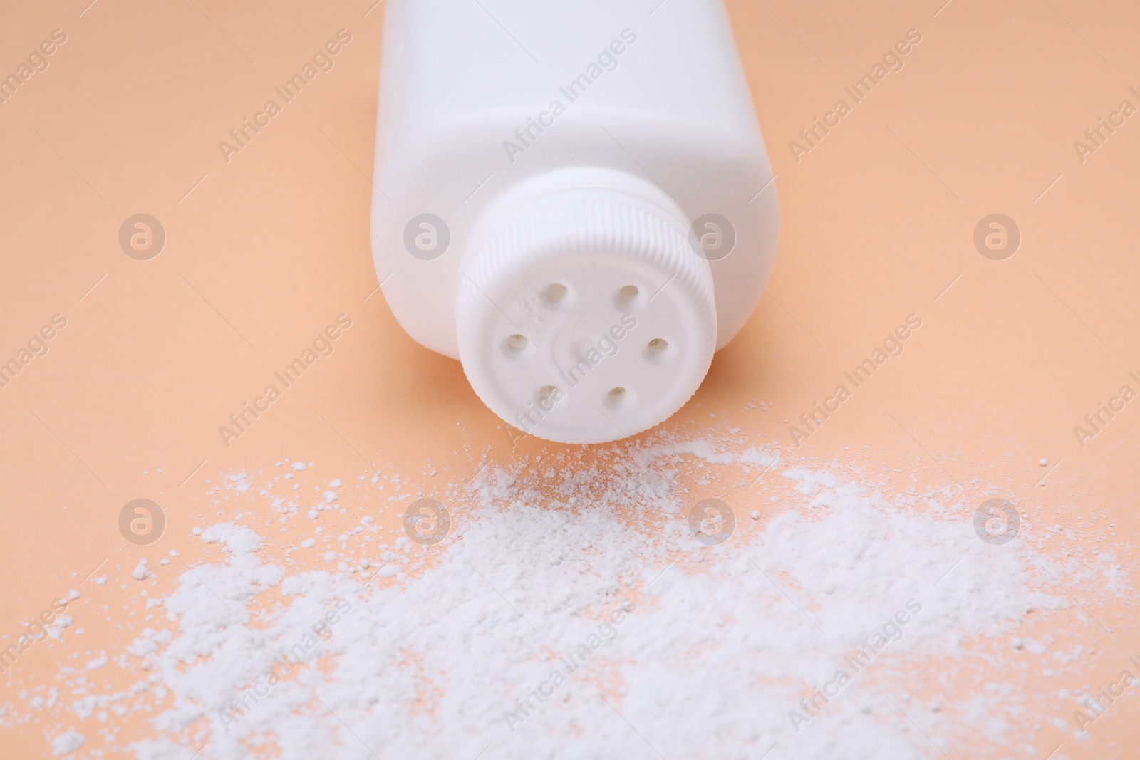 Photo of Bottle and scattered dusting powder on pale coral background, closeup. Baby cosmetic product