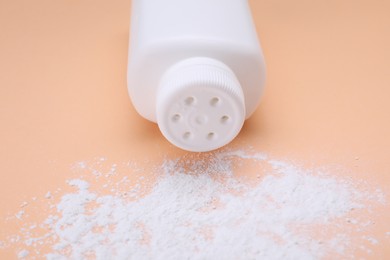 Bottle and scattered dusting powder on pale coral background, closeup. Baby cosmetic product
