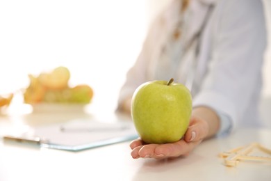 Image of Nutritionist with apple at desk in office, closeup. Space for text