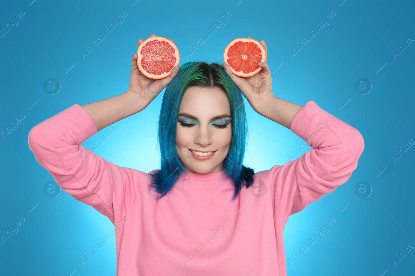 Photo of Young woman with bright dyed hair holding grapefruit on light blue background