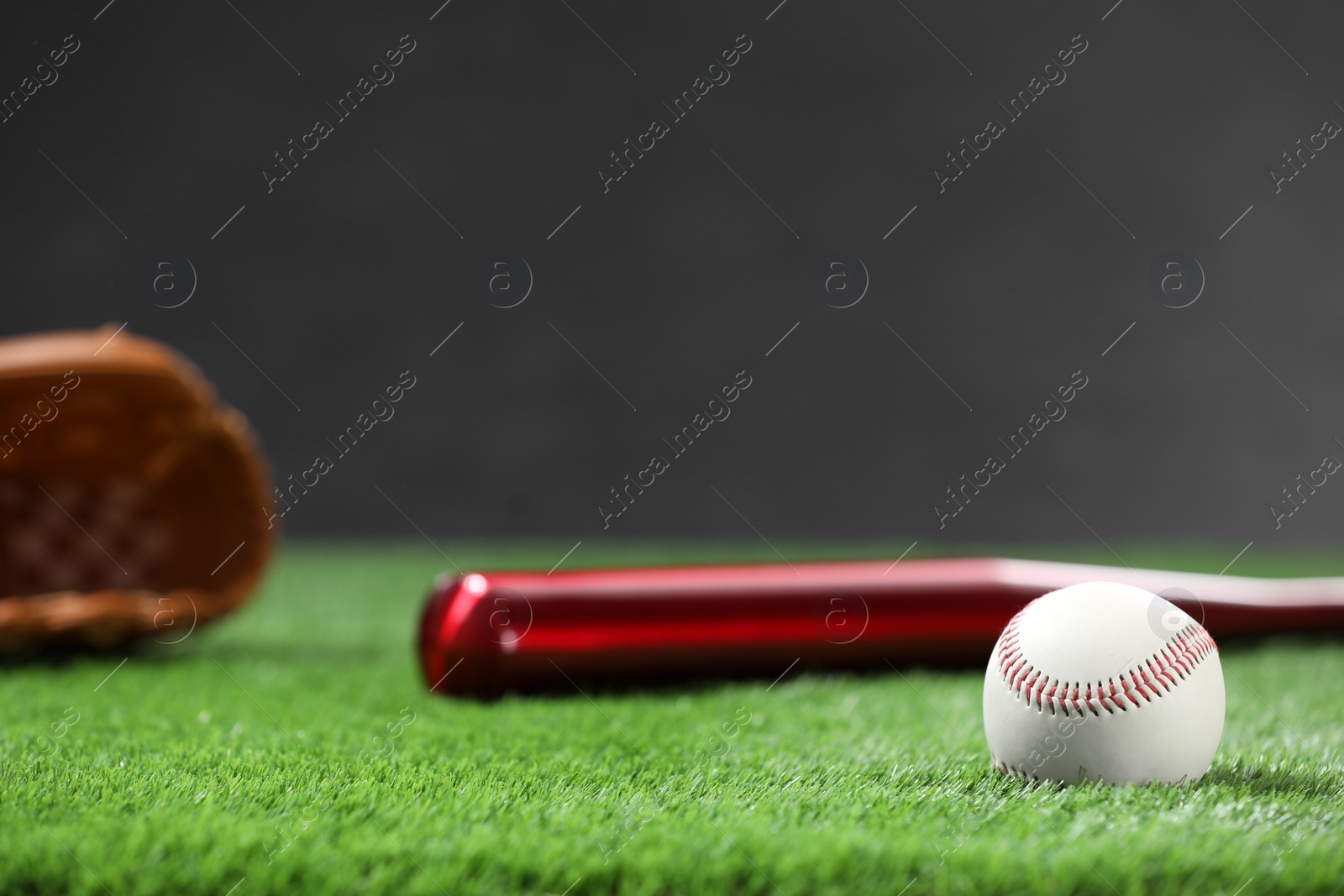 Photo of Baseball bat and ball on green grass against dark background. Space for text