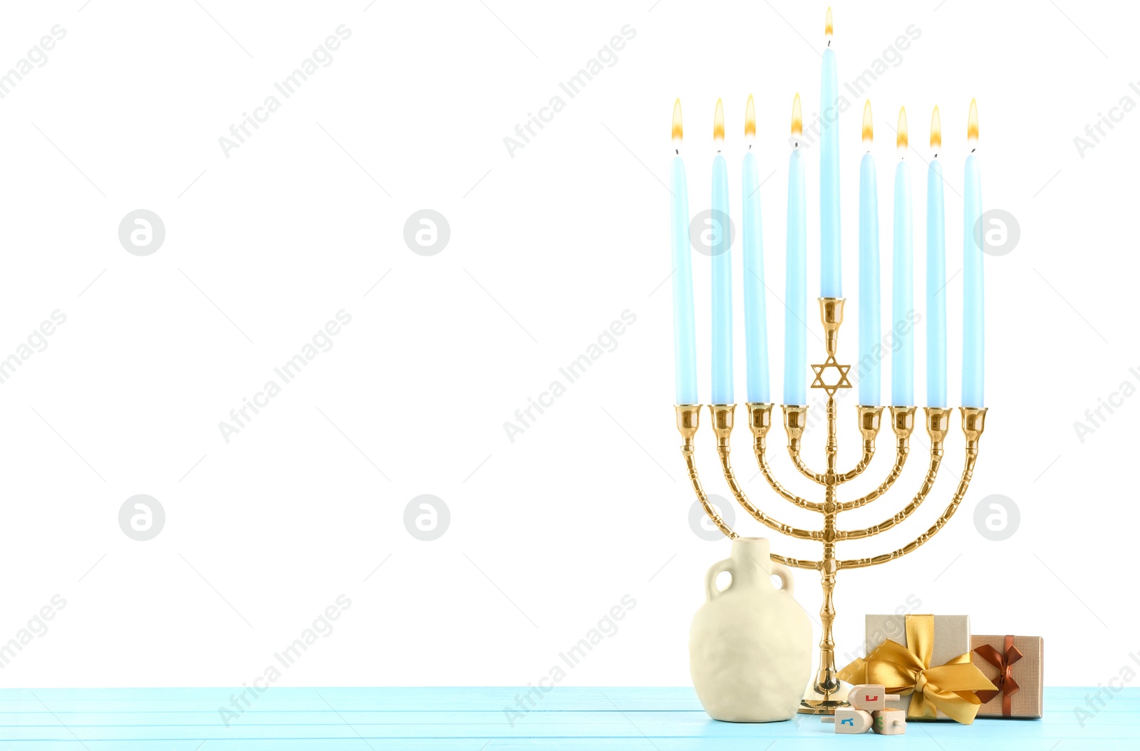 Photo of Hanukkah celebration. Menorah, dreidels, vase and gift boxes on light blue wooden table against white background