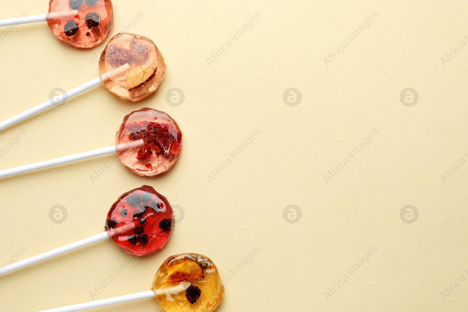 Photo of Sweet colorful lollipops with berries on beige background, flat lay. Space for text