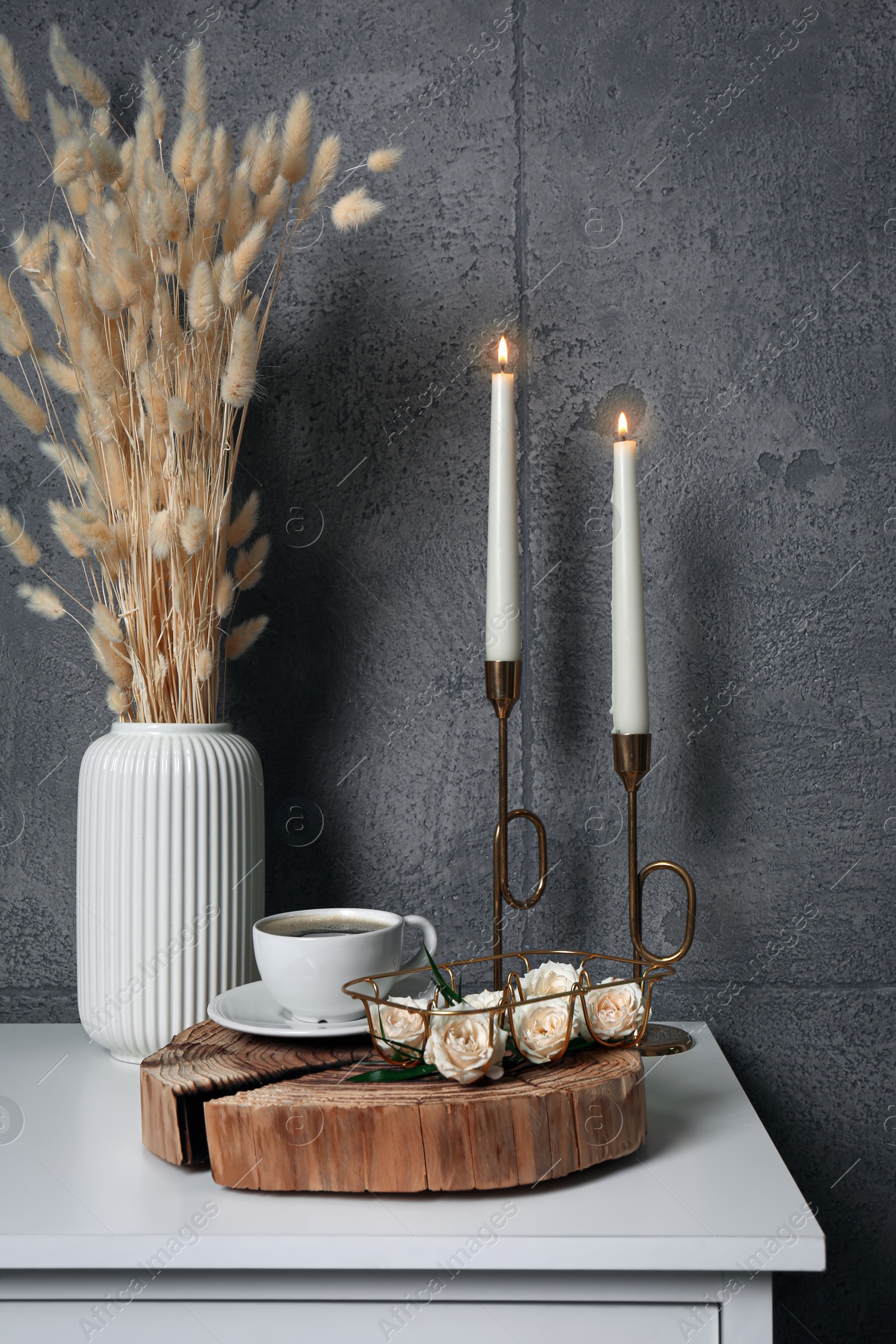 Photo of Cup of coffee, vase and other decor on white table near grey wall indoors. Interior design