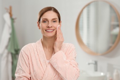 Beautiful woman removing makeup with cotton pad indoors, space for text