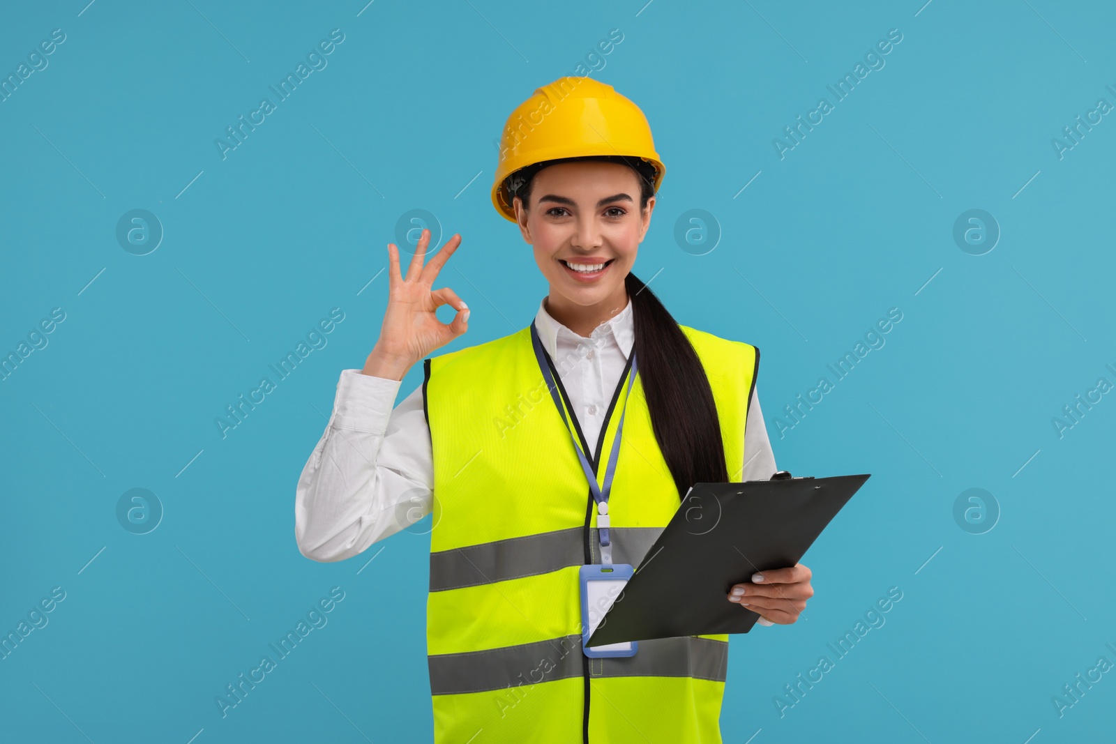 Photo of Engineer in hard hat showing ok gesture on light blue background