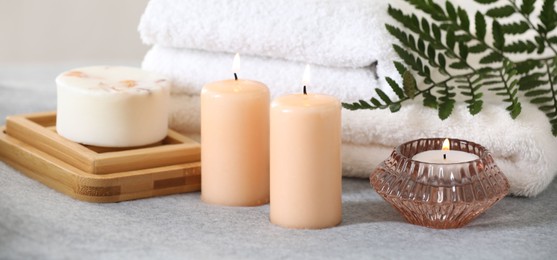 Photo of Spa composition. Burning candles, soap and towels on soft grey surface