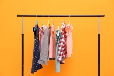 Rack with stylish child clothes on color background