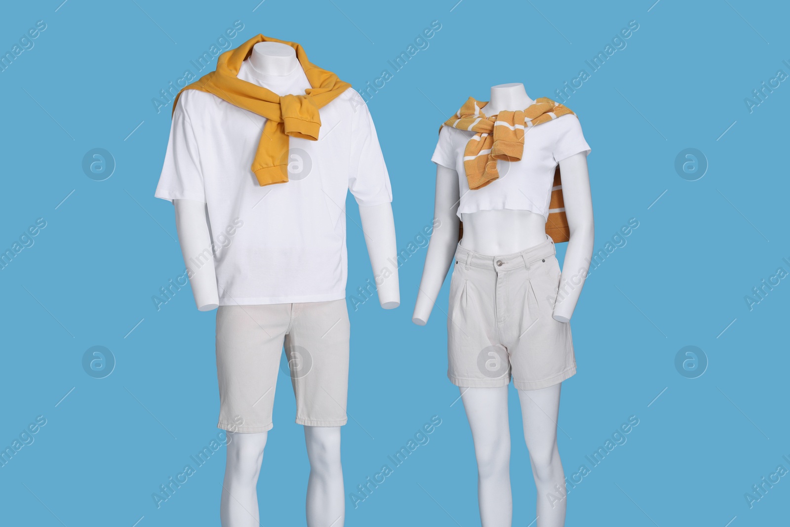Photo of Female and male mannequins dressed in white t-shirts, stylish shorts and orange sweaters on light blue background