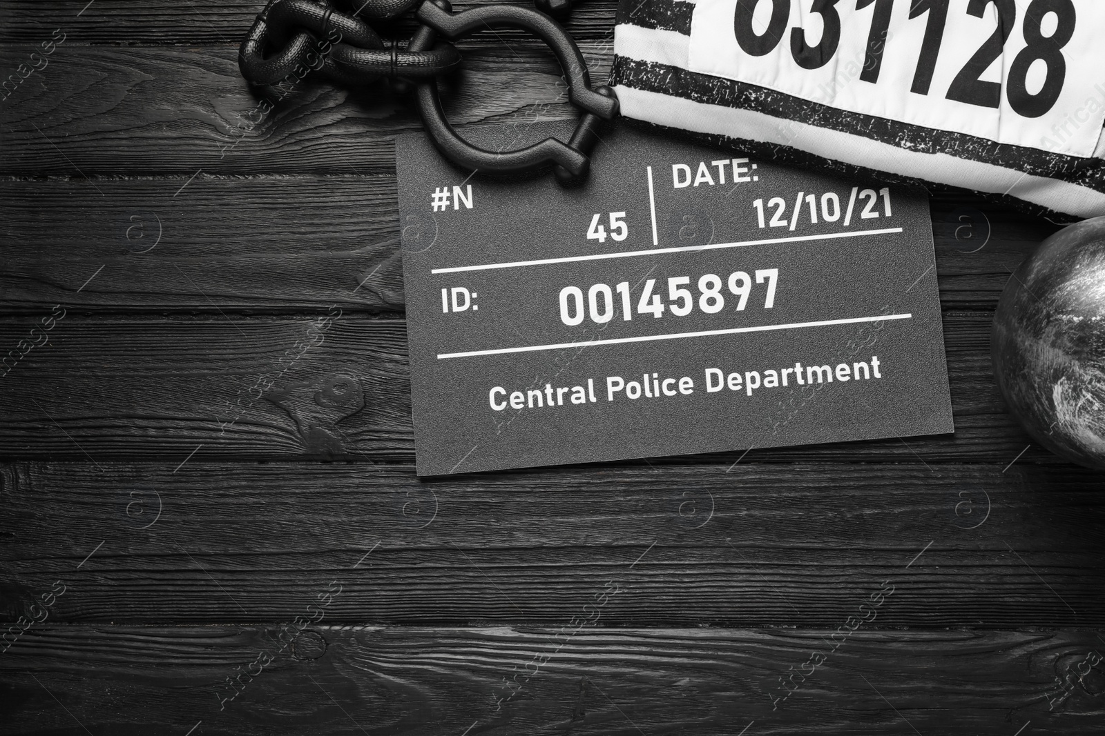Photo of Metal ball with chain, prison uniform and mugshot letter board on black wooden table, flat lay. Space for text