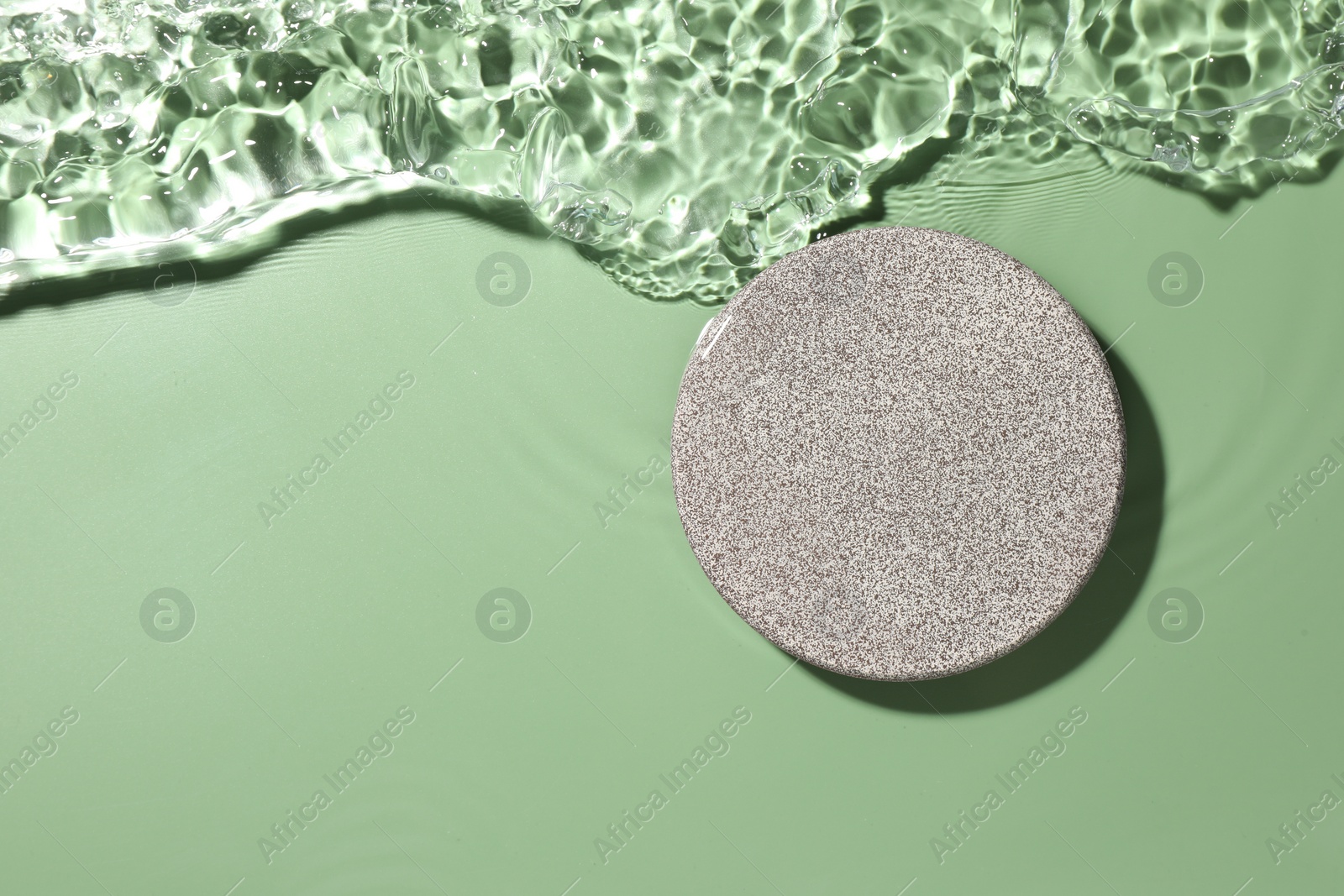 Photo of Presentation of product. Stone podium in water on green background, top view. Space for text