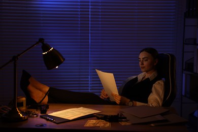 Professional detective working with documents at table in office at night