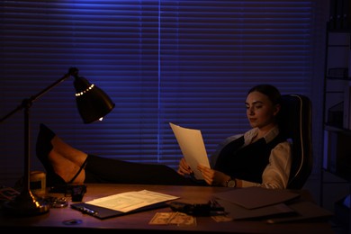 Photo of Professional detective working with documents at table in office at night