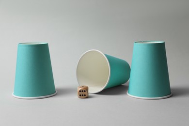 Three paper cups and dice on light grey background. Thimblerig game