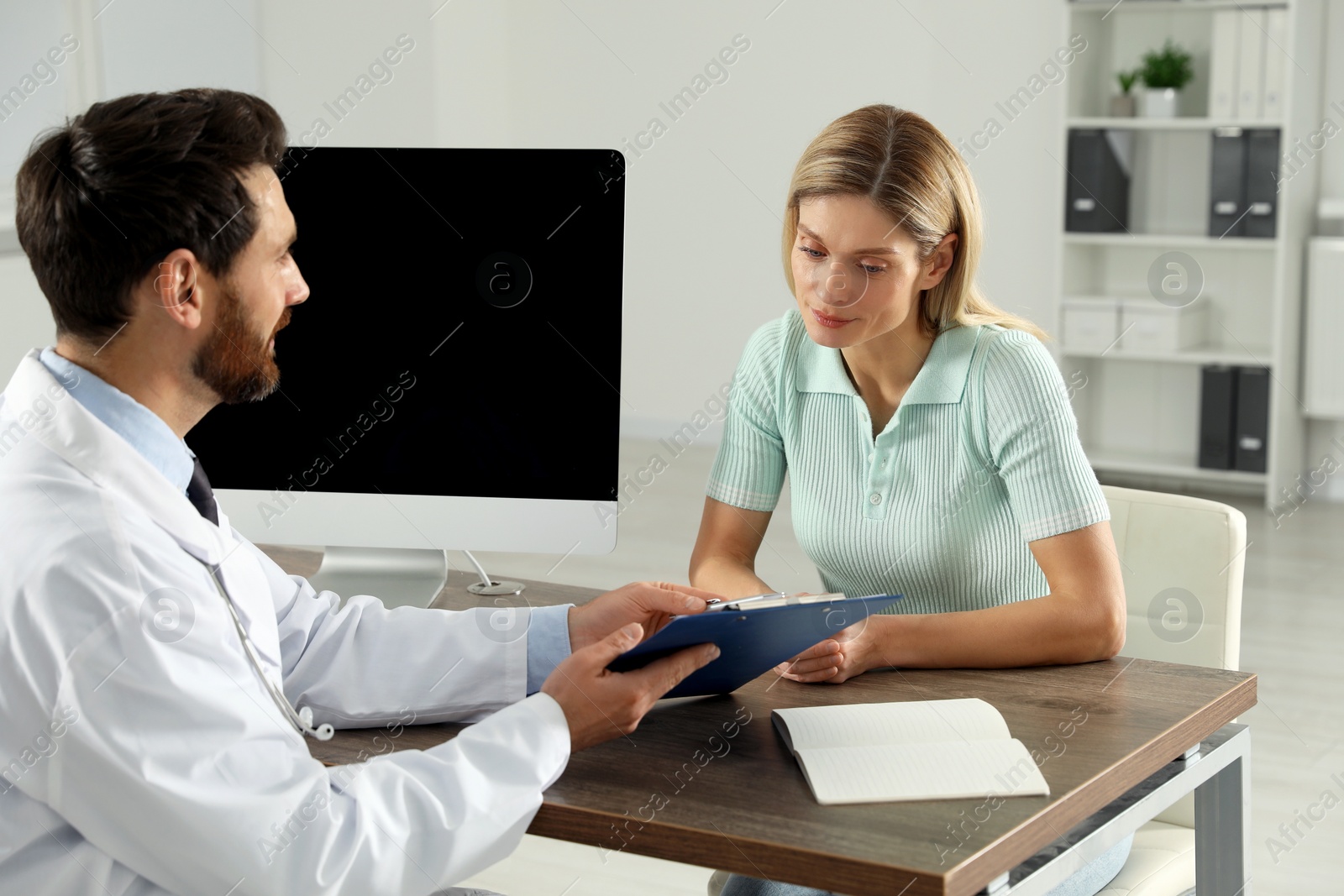 Photo of Doctor consulting patient at wooden table in clinic