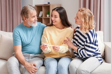 Photo of Happy woman showing her parents pregnancy test at home. Grandparents' reaction to future grandson