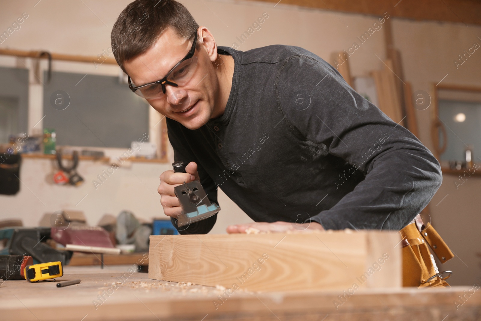 Photo of Professional carpenter grinding wooden plank with jack plane in workshop