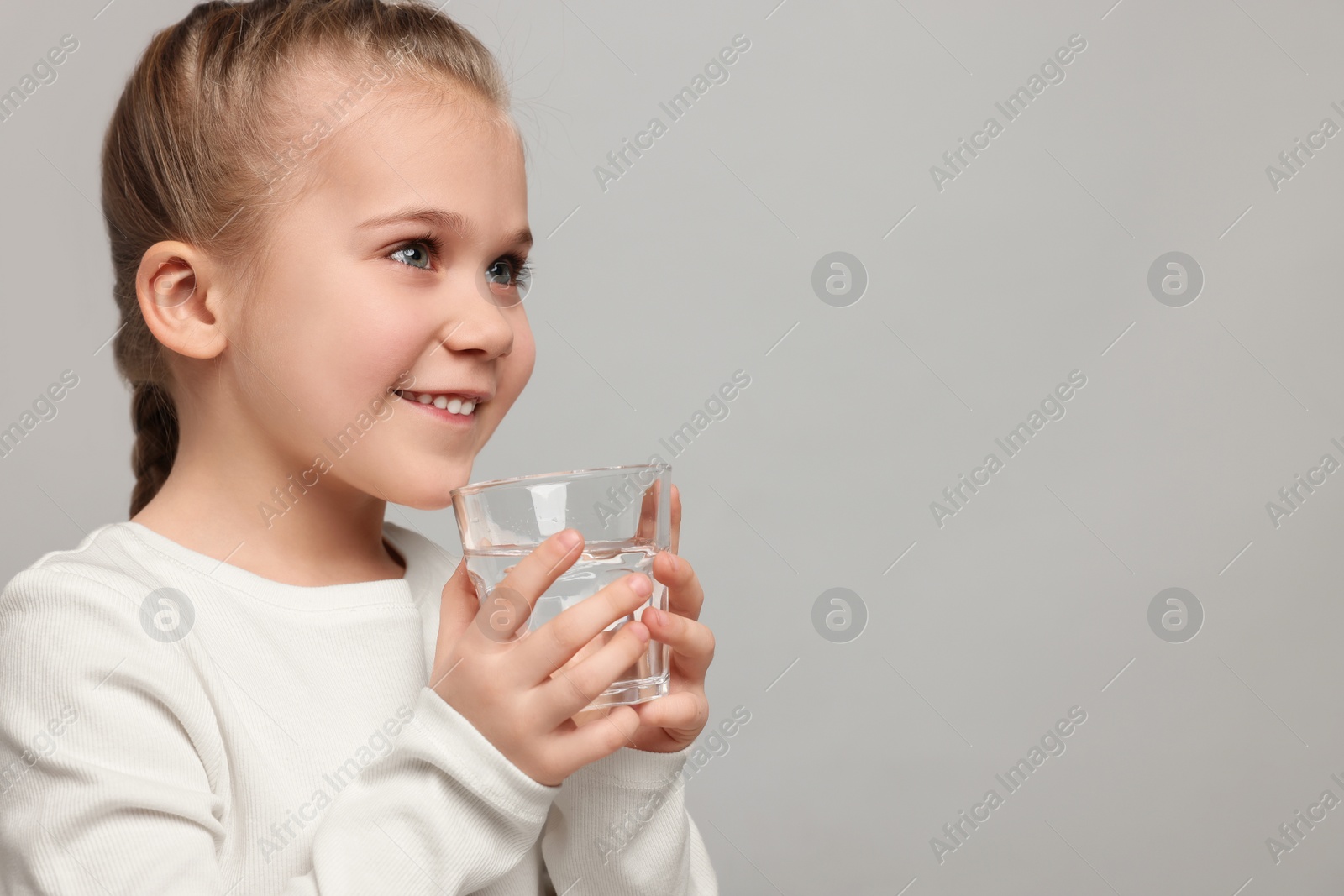 Photo of Happy little girl holding glass of fresh water on light grey background, space for text