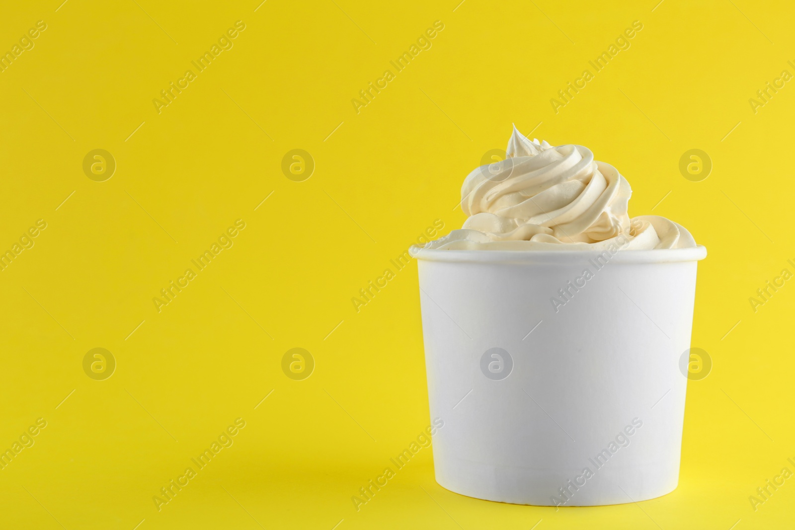 Photo of Cup with tasty frozen yogurt on yellow background. Space for text